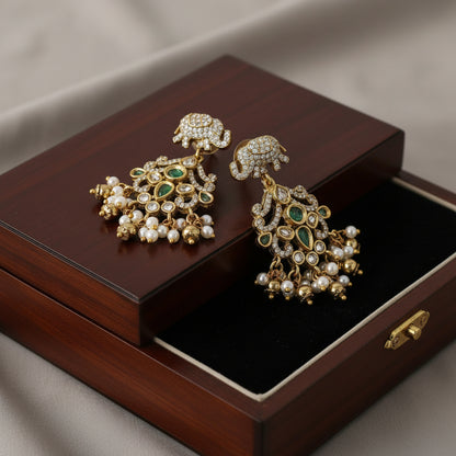 Ornate gold earrings with green stones on a wooden jewelry box.
