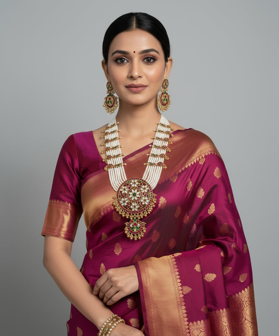 Woman wearing a traditional maroon saree with gold patterns and jewelry on a gray background