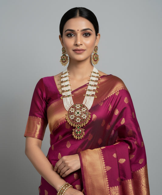 Woman wearing a traditional maroon saree with gold patterns and jewelry on a gray background