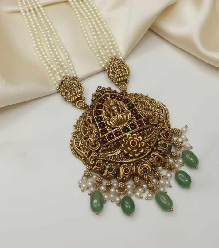 Ornate gold necklace with pearls and green stones on a white background