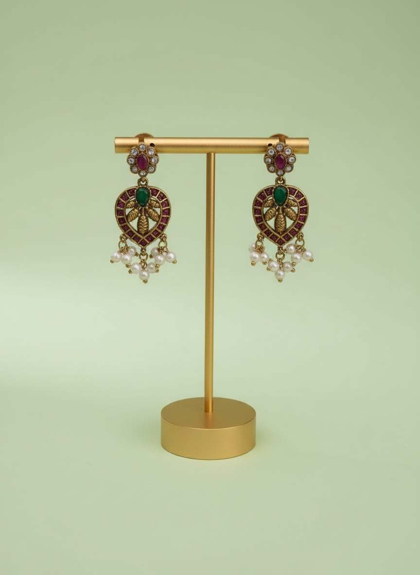 Pair of ornate earrings with gemstones on a gold stand against a light green background