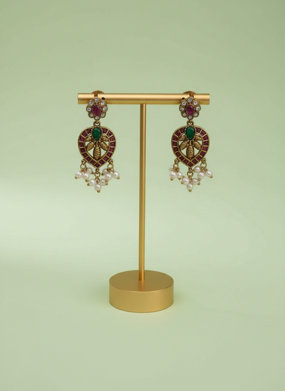 Pair of ornate earrings with gemstones on a gold stand against a light green background