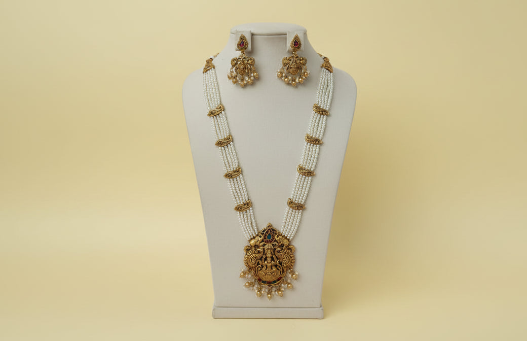 Gold necklace and earrings on a white stand with a pink background