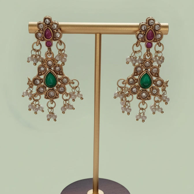 Gold earrings with gemstones on a wooden stand against a white background
