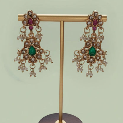Gold earrings with gemstones on a wooden stand against a white background