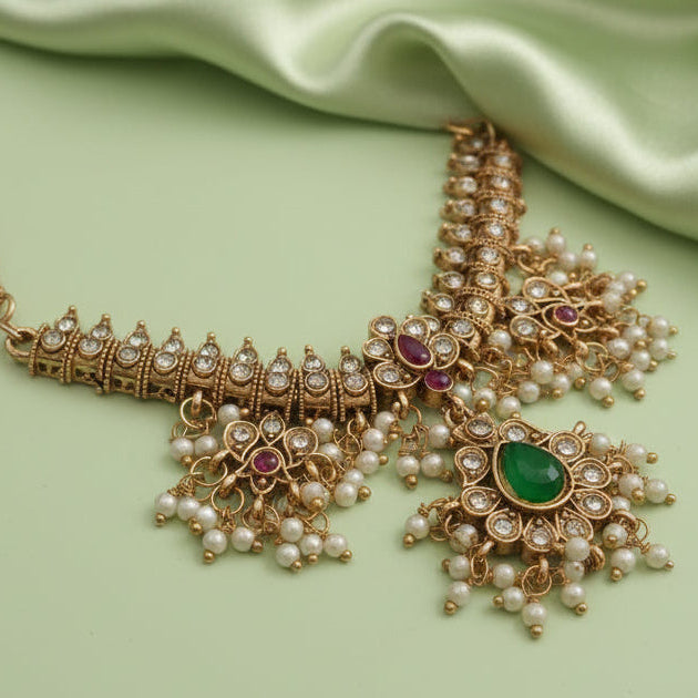 Ornate gold necklace with pearls and gemstones on a light green fabric background