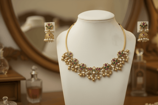 This gold-toned necklace and earring set features pink and green lotus motifs enhanced by delicate pearl hangings.
